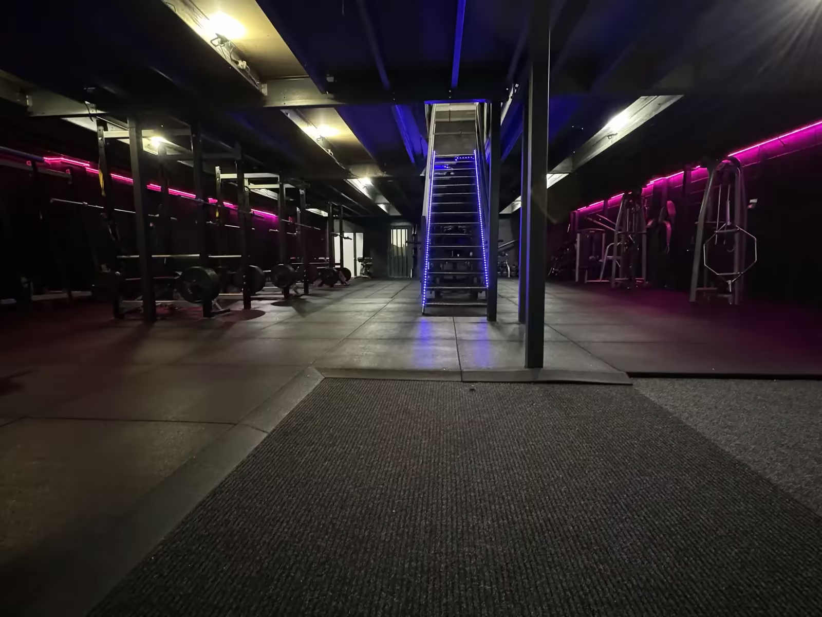 The gym floor under violet neon, stairs to the mezzanine
