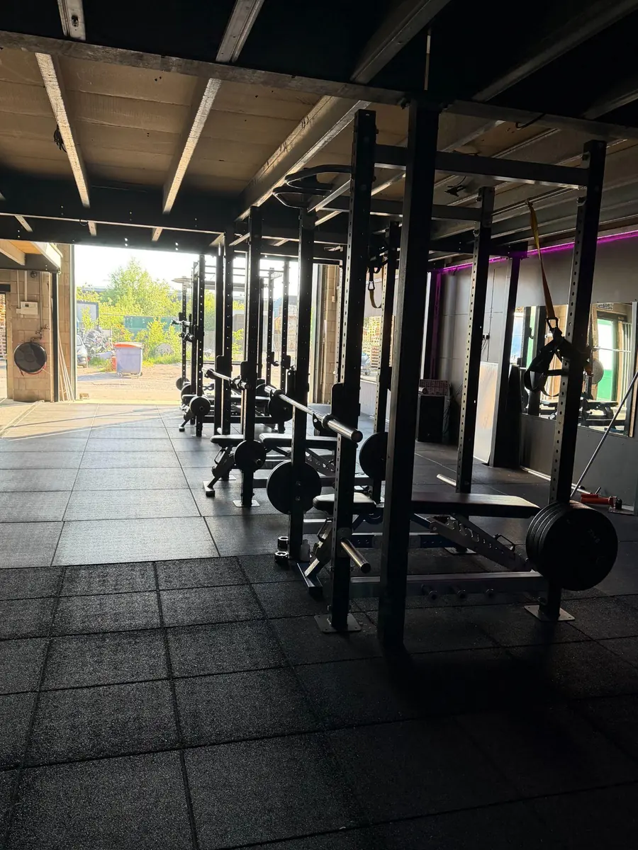 Squat racks and barbells along the rig at Lycan Strength, shutter open to the yard