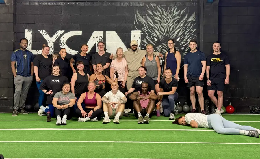 Members sitting on the turf in front of the Lycan wall after a class